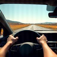 Image showing hands on a steering wheel with a clear road stretching ahead towards a beautiful horizon.