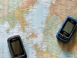 A stack of detailed regional maps, a local guide book, and a modern GPS device, representing the provision of essential navigation tools.